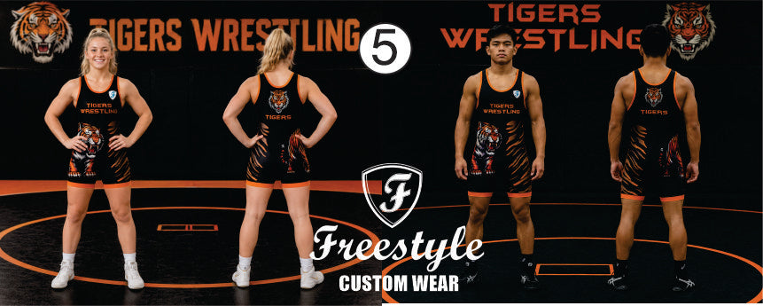 Four wrestlers wearing matching black and orange Freestyle Custom Wear singlet outfits are shown from front and back views on a wrestling mat background with 'Tigers Wrestling 5' branding.